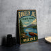 A vintage-style metal sign for Rangeley Lake State Park in Maine, featuring a scenic illustration of a lake, mountains, and a red canoe.