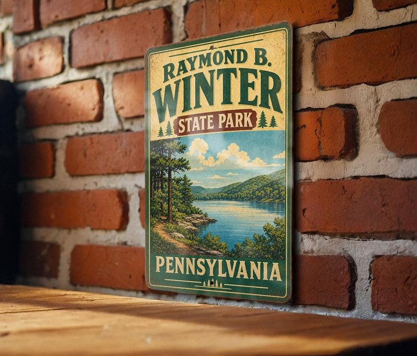 A vintage-style metal sign for Raymond B. Winter State Park in Pennsylvania, featuring a scenic landscape with a lake and mountains.