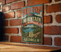 A vintage-style metal sign for Red Top Mountain State Park in Georgia, featuring a scenic landscape with a mountain, lake, and trees.