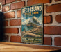 A vintage-style metal sign for Reed Island State Park in Washington, featuring a scenic landscape with a mountain, trees, and a body of water.
