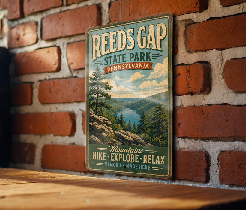 A vintage-style metal sign for Reed's Gap State Park in Pennsylvania, featuring a scenic mountain landscape with pine trees and a lake.