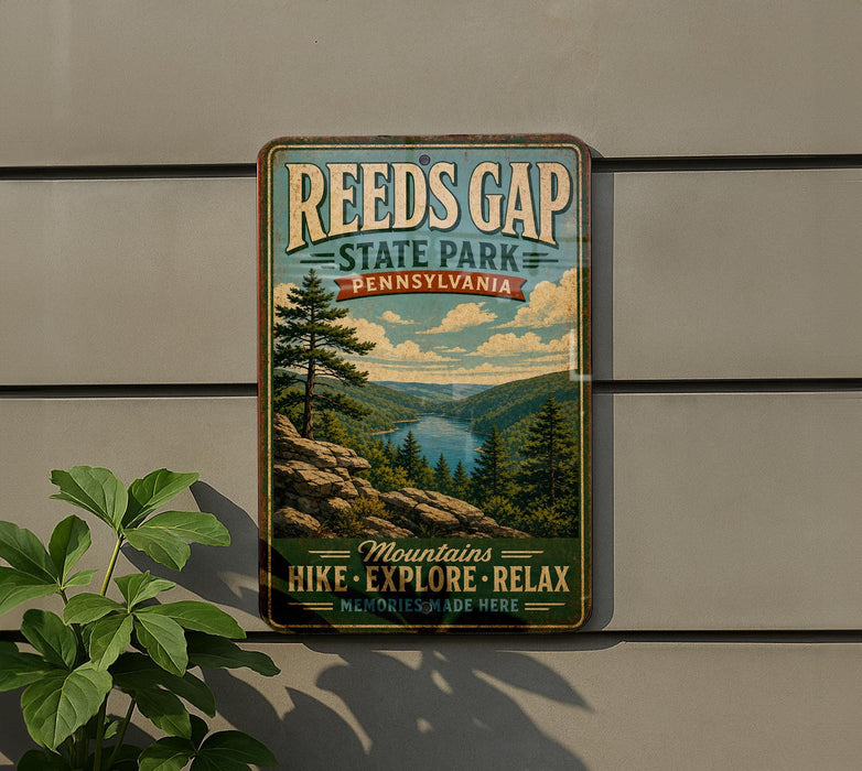 A vintage-style metal sign for Reeds Gap State Park in Pennsylvania, featuring a scenic mountain landscape with pine trees and a lake.