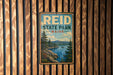 A vintage metal sign for Reid State Park in Maine, featuring a scenic landscape with pine trees, a lake, and mountains.