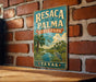 A vintage-style metal sign for Resaca de la Palma State Park in Texas, featuring a palm tree and a bird, is displayed on a brick wall.