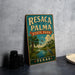 A vintage-style sign for Resaca de la Palma State Park in Texas, featuring a palm tree and a bird in flight, is displayed on a gray countertop next to some black camera lenses.