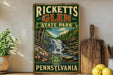 A vintage-style sign for Ricketts Glen State Park in Pennsylvania, featuring a scenic image of a waterfall surrounded by trees and flowers.