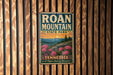 A vintage-style metal sign for Roan Mountain State Park in Tennessee, featuring a scenic landscape with mountains, pine trees, and pink flowers.