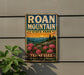 A vintage-style metal sign for Roan Mountain State Park in Tennessee, featuring a scenic landscape with mountains, pine trees, and pink flowers.