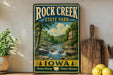 A vintage-style sign for Rock Creek State Park in Iowa, featuring a scenic landscape with a waterfall and lush greenery.