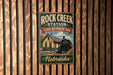 A vintage-style metal sign for Rock Creek Station, a State Historical Park in Nebraska, featuring a train and a building.