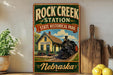 A vintage-style sign for Rock Creek Station, a State Historical Park in Nebraska, featuring an illustration of a train station with a locomotive.
