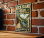 A vintage-style metal sign for Rock Island Trail State Park in Illinois, featuring a scenic image of a bridge and a river.