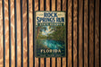A vintage-style metal sign for Rock Springs Run State Reserve in Florida, featuring a tropical landscape with palm trees and a river.