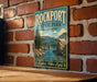 A vintage-style metal sign for Rockport State Park in Washington, featuring a scenic landscape with a bridge and mountains.