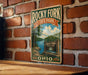 A vintage-style metal sign for Rocky Fork State Park in Ohio, featuring a scenic landscape with a river and forest.
