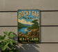 A vintage-style sign for Rocky Gap State Park in Maryland, featuring a scenic landscape with mountains, a lake, and a pine tree.