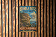 A vintage metal sign for Roman Nose State Park in Oklahoma, featuring a scenic image of a cliff and a blue sky with clouds.