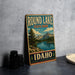 A vintage-style sign for Round Lake State Park in Idaho, featuring a scenic mountain landscape and a lake.