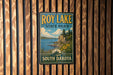 A vintage-style metal sign for Roy Lake State Park in South Dakota, featuring a scenic landscape with a lake, mountains, and trees.