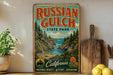 A vintage-style metal sign for Russian Gulch State Park in California, featuring a scenic landscape with a waterfall and pine trees.