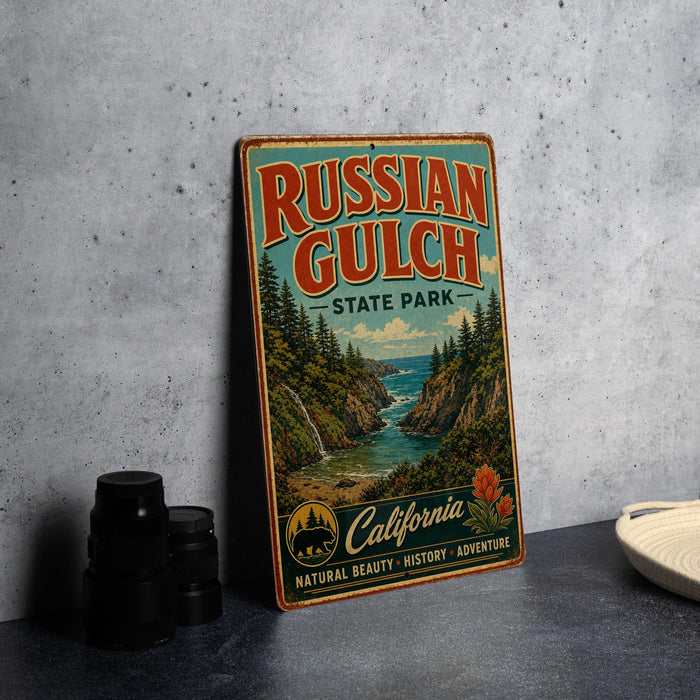 A vintage-style metal sign for Russian Gulch State Park, featuring a scenic landscape with a river, mountains, and pine trees.