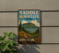 A vintage-style metal sign for Saddle Mountain State Natural Area in Oregon, featuring a scenic mountain landscape with pine trees, a lake, and a path leading to the mountain.