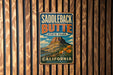 A vintage metal sign for Saddleback Butte State Park in California, featuring a mountain landscape with flowers.
