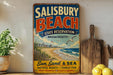 A vintage-style metal sign for Salisbury Beach State Reserve in Massachusetts, featuring a beach scene with a lighthouse and birds, along with the text "Sun, Sand & Sea Natural Beauty - Family Fun Make Memories it last a Lifetime".
