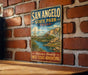 A vintage-style metal sign for San Angelo State Park in Texas, featuring a scenic landscape with a river and mountains.