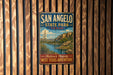 A vintage-style metal sign for San Angelo State Park in Texas, featuring a scenic landscape with a desert and a body of water.