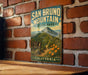 A vintage metal sign for San Bruno Mountain State Park in California, featuring a scenic mountain landscape with a trail leading through the forest.