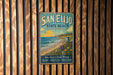 A vintage metal sign for San Elijo State Beach, California, featuring a beach scene with a lifeguard tower and a sunset over the ocean.