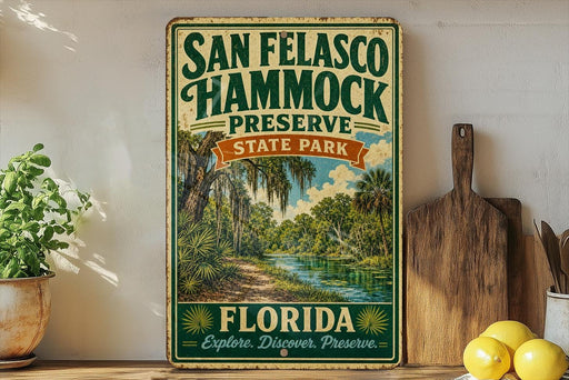 A vintage-style sign for San Francisco Hammock Preserve, featuring a tropical landscape with palm trees and a river, is displayed on a shelf next to a wooden cutting board and some lemons.