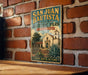 A vintage-style metal sign for San Juan Bautista State Historic Park in California, featuring an illustration of a historic building and a palm tree.