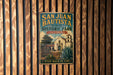A vintage-style metal sign for San Juan Bautista State Historic Park in California, featuring an illustration of a historic building and a palm tree.
