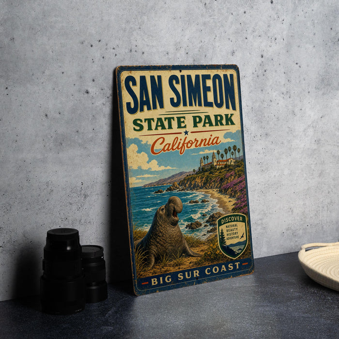 A vintage metal sign for San Simeon State Park in California, featuring a scenic image of a seal on the beach and the ocean.