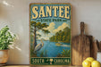 A vintage-style sign for Santee State Park in South Carolina, featuring a serene landscape with a crane, a boat on the water, and a backdrop of trees and a blue sky.