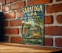 A vintage-style metal sign for Saratoga Spa, New York, featuring an illustration of the spa and its surroundings.