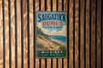 A vintage metal sign for Saugatuck Dunes State Park in Michigan, featuring a scenic beach landscape with pine trees and a body of water.