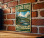 A vintage metal sign for Savage River State Forest in Maryland, featuring a scenic landscape with a river and pine trees.