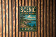 A vintage-style metal sign for Scenic State Park in Minnesota, featuring a scenic landscape with pine trees, a lake, and mountains.