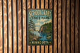 A vintage metal sign for Schoolcraft State Park in Minnesota, featuring a scenic landscape with pine trees, a lake, and mountains.
