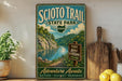 a vintage-style sign for the Scio Trail State Park in Ohio, with a scenic illustration of a river and mountains. The sign also includes the words "Adventure Awaits" and "Nature - History - Memories".