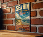 A vintage metal sign for Sea Rim State Park in Texas, featuring a beach scene and a lighthouse, is displayed on a brick wall.