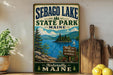A vintage-style sign for Sebago Lake State Park in Maine, featuring a scenic landscape with pine trees, mountains, and a lake.