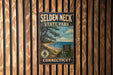 A vintage metal sign for Selden Neck State Park in Connecticut, featuring a scenic landscape with a beach, pine trees, and a blue sky with clouds.