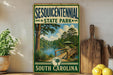 A vintage-style metal sign for Sesquicentennial State Park in South Carolina, featuring a scenic landscape with a bridge and trees.