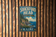 A vintage metal sign for Shackford Head State Park in Maine, featuring a scenic landscape with a rocky cliff, pine trees, and a body of water.