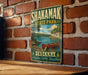 A vintage-style metal sign for Shakamak State Park in Indiana, featuring a scenic illustration of a canoe on a lake surrounded by trees.