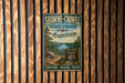 A vintage metal sign for Shawme-Crowell State Forest in Massachusetts, featuring a scenic image of a forest and a lake.